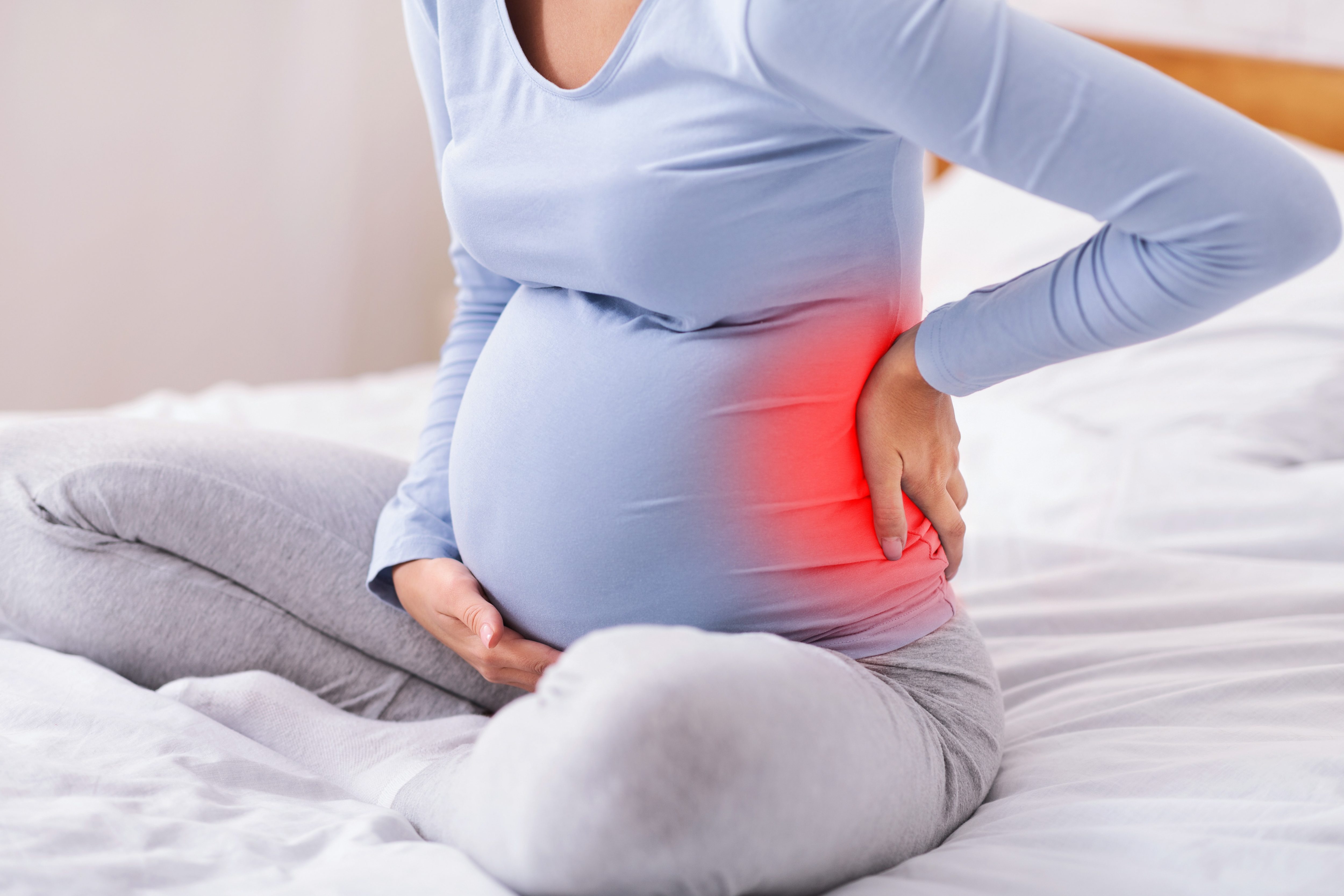 Unrecognizable Pregnant Lady Touching Back Sitting On Bed